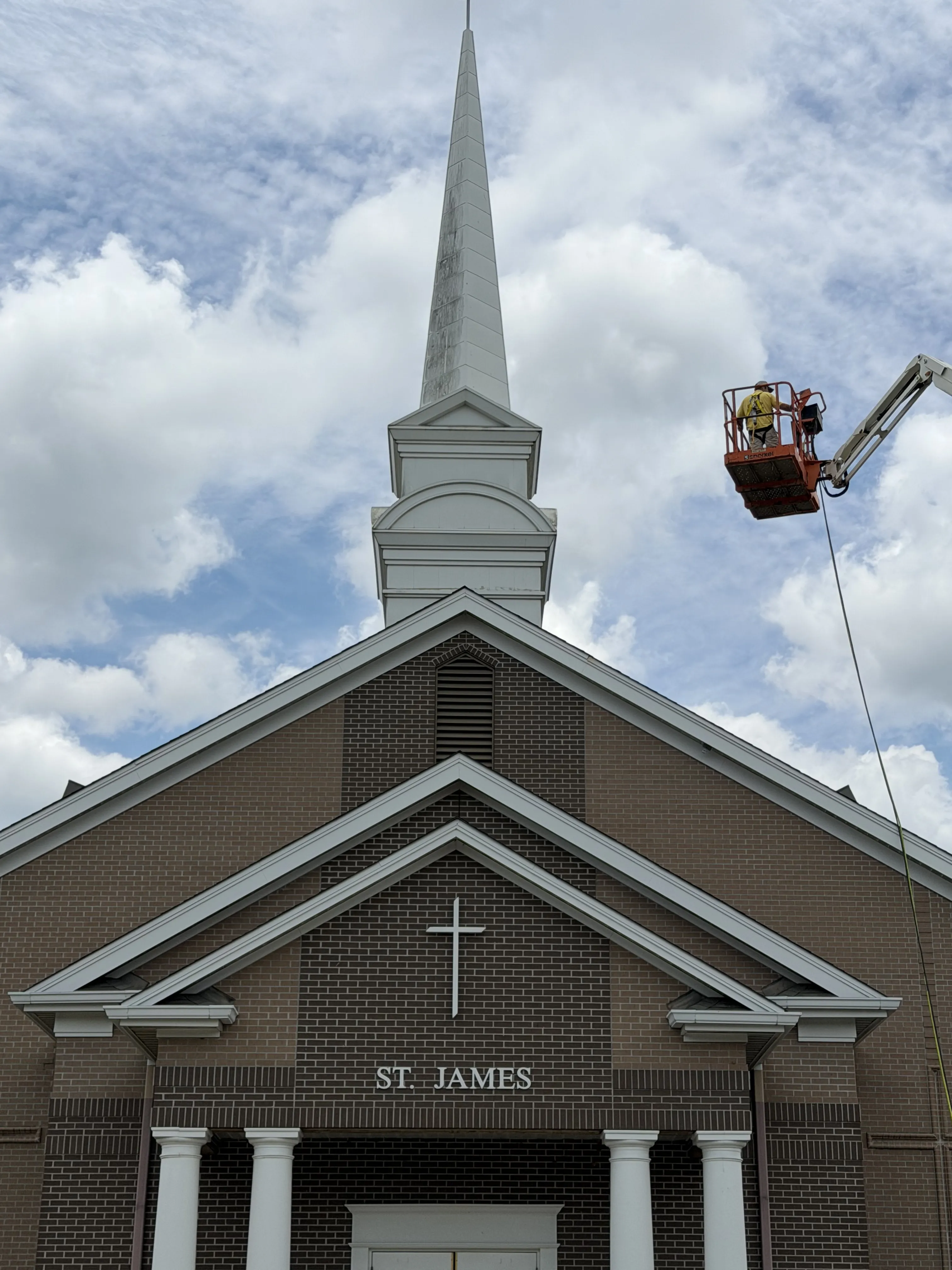 HoneyBee soft-washing a church steeple from a lift